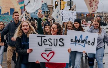 Jézus neét viselő transzparenssel menetelő vidám emberek
